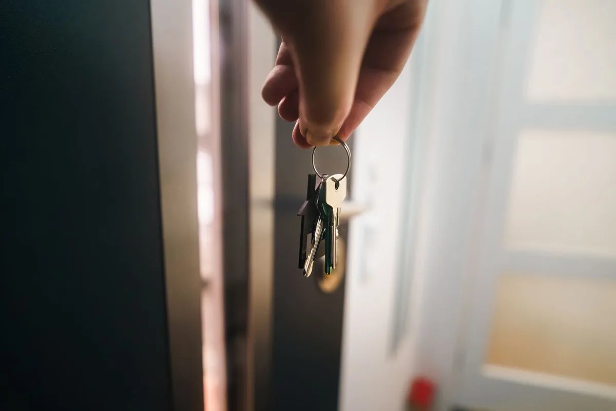 Una mano sostiene las llaves junto a la entrada de una vivienda